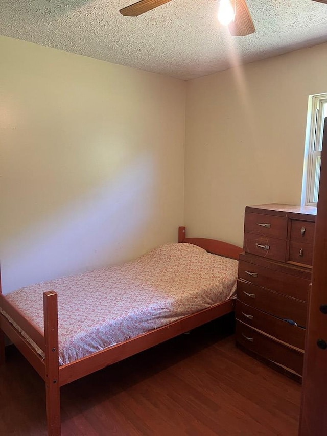 bedroom featuring dark wood finished floors, a ceiling fan, and a textured ceiling