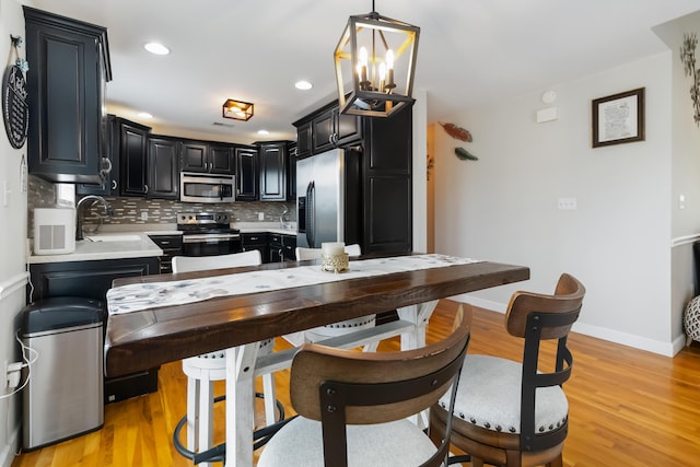 kitchen featuring light wood-style floors, dark cabinetry, tasteful backsplash, light countertops, and appliances with stainless steel finishes