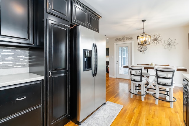 kitchen with hanging light fixtures, stainless steel fridge, light wood-style floors, light countertops, and dark cabinetry