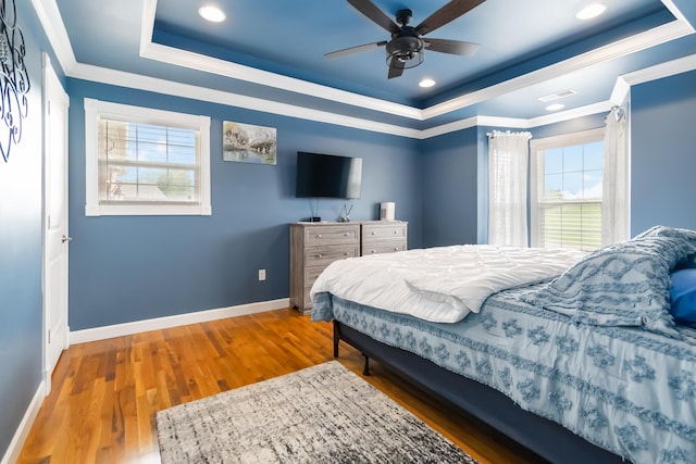 bedroom with visible vents, a raised ceiling, wood finished floors, and multiple windows