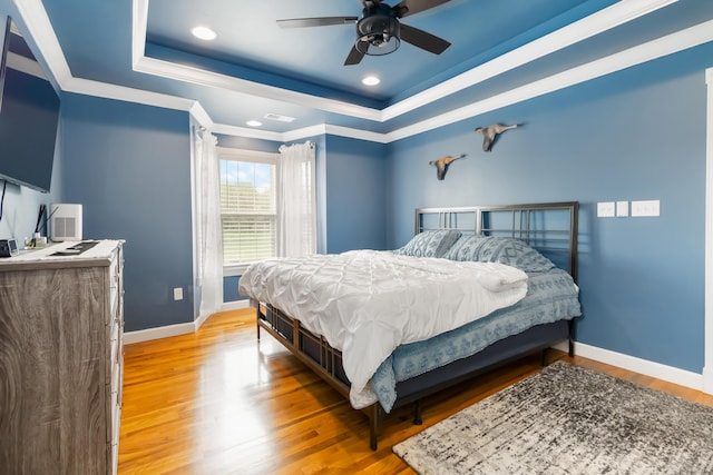 bedroom featuring baseboards, a raised ceiling, ornamental molding, and light wood-style flooring
