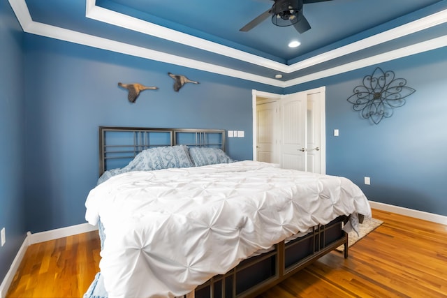 bedroom featuring crown molding, baseboards, wood finished floors, and a tray ceiling