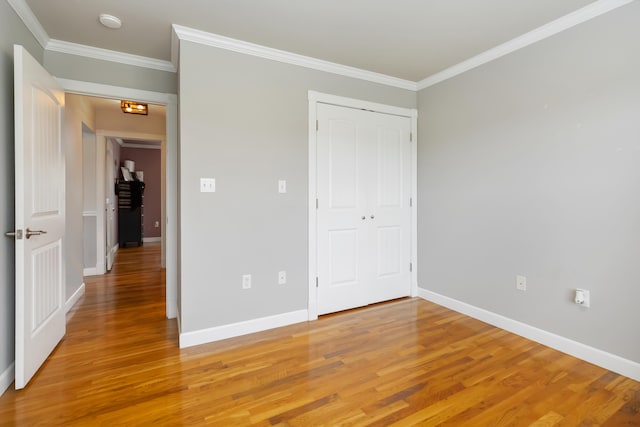unfurnished bedroom with baseboards, ornamental molding, a closet, and light wood-style flooring