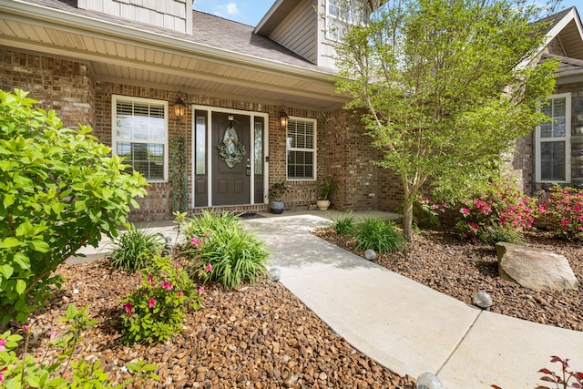 entrance to property with brick siding, a porch, and a shingled roof