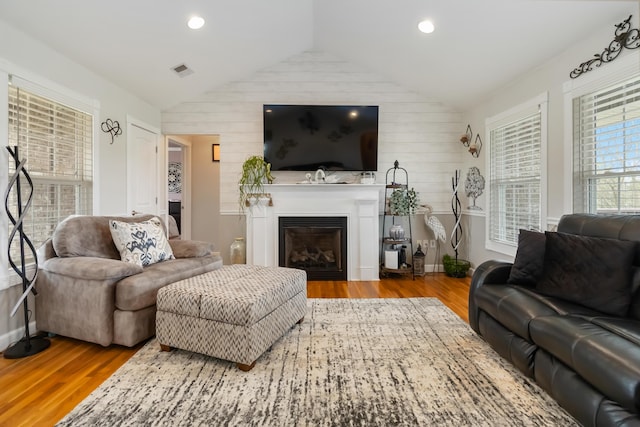 living room with lofted ceiling, visible vents, wood finished floors, and a glass covered fireplace