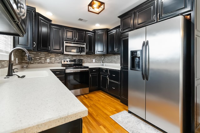 kitchen with a sink, visible vents, light wood-style flooring, appliances with stainless steel finishes, and dark cabinets