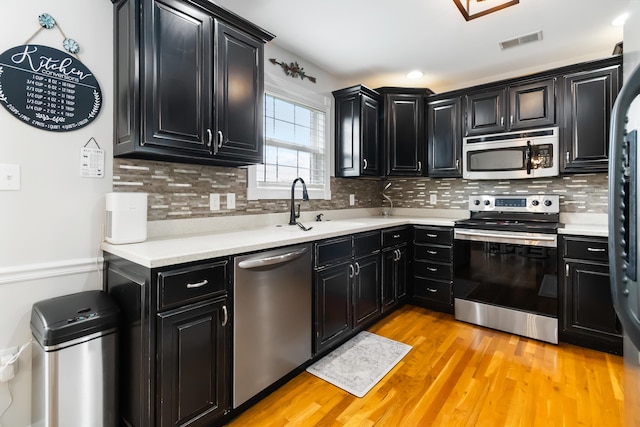 kitchen with light wood-style floors, appliances with stainless steel finishes, dark cabinetry, a sink, and visible vents