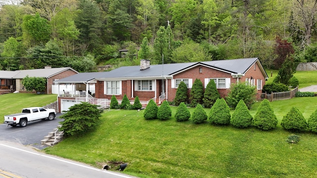 ranch-style home with brick siding, driveway, a chimney, and a front lawn
