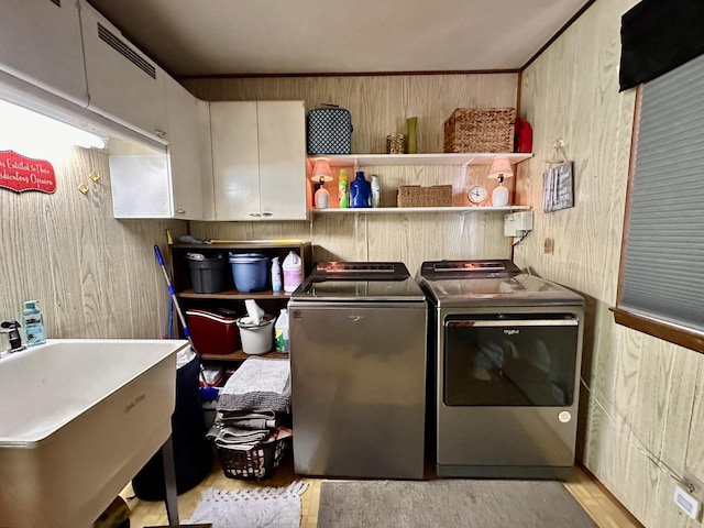 clothes washing area with visible vents, washing machine and clothes dryer, wood walls, cabinet space, and a sink