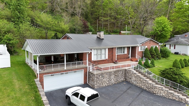view of front facade featuring a front lawn, an attached garage, a chimney, metal roof, and a porch