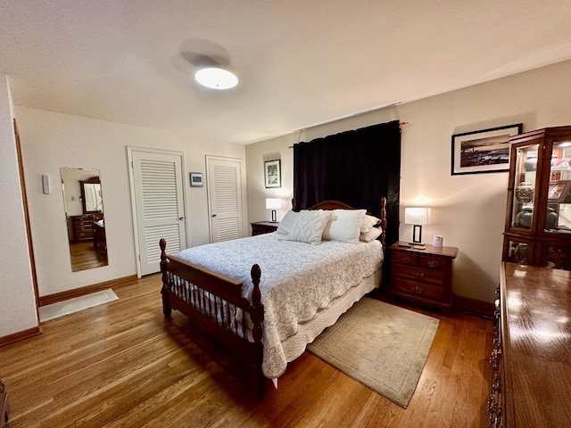 bedroom featuring baseboards, light wood-style flooring, and two closets