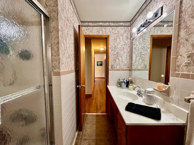 full bathroom with vanity, wainscoting, tile walls, wallpapered walls, and a stall shower