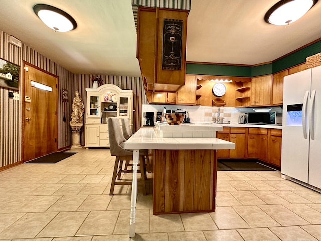 kitchen with brown cabinetry, open shelves, black microwave, white refrigerator with ice dispenser, and tile counters