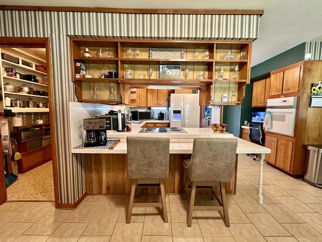 kitchen with oven, open shelves, tile countertops, a peninsula, and fridge with ice dispenser