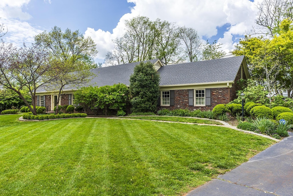 view of front of property featuring roof with shingles, a front yard, and brick siding