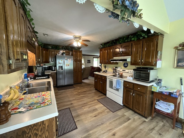kitchen with a sink, light countertops, stainless steel appliances, light wood-style flooring, and under cabinet range hood