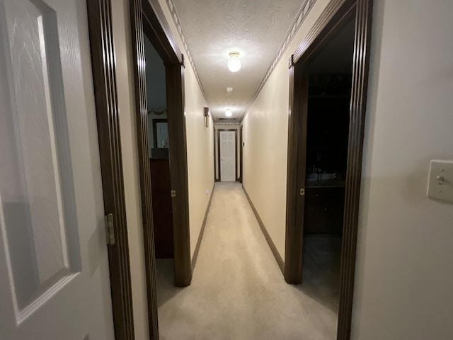 hallway featuring baseboards, a textured ceiling, and ornamental molding