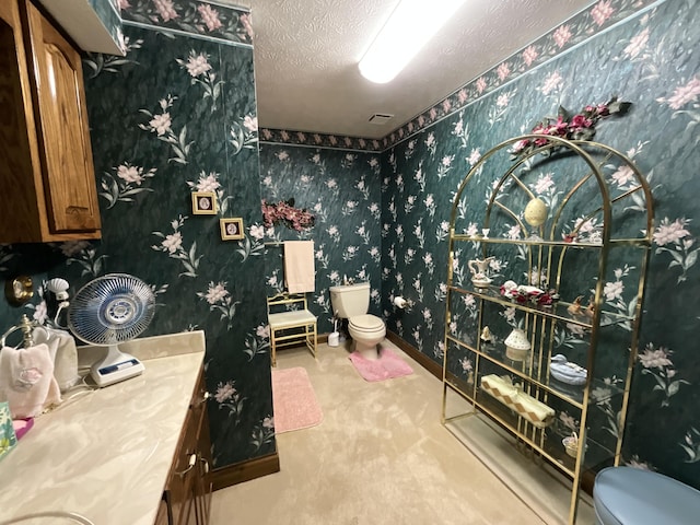 bathroom featuring toilet, vanity, a textured ceiling, and wallpapered walls