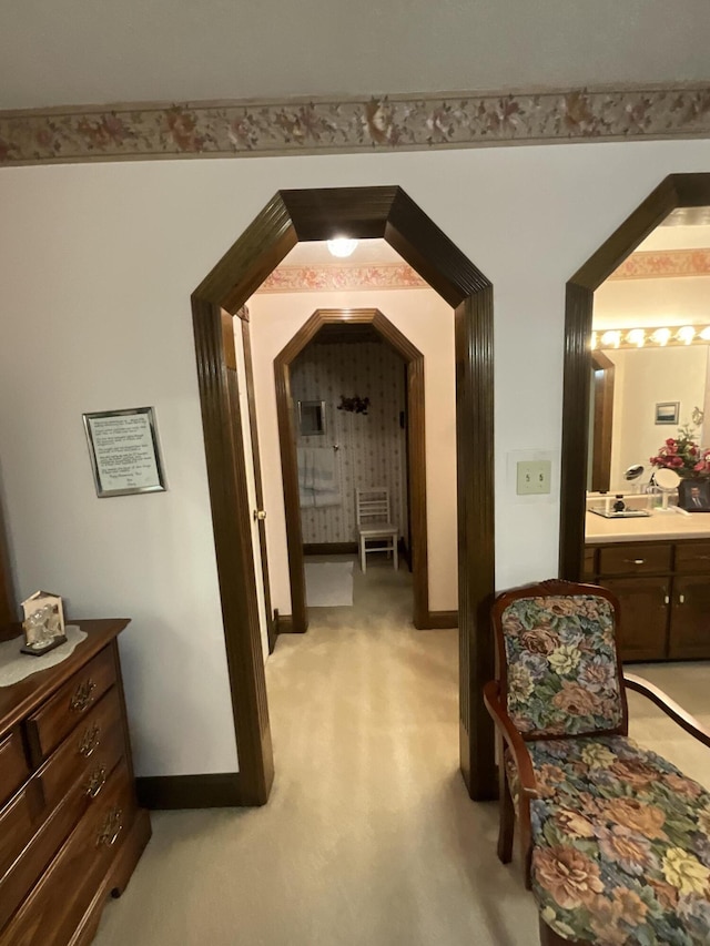 hallway with baseboards, a sink, and light colored carpet