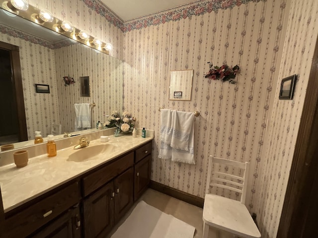 bathroom with baseboards, vanity, and wallpapered walls