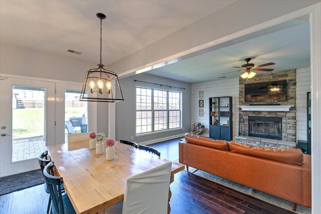 dining area featuring a fireplace, visible vents, ceiling fan with notable chandelier, and dark wood-type flooring