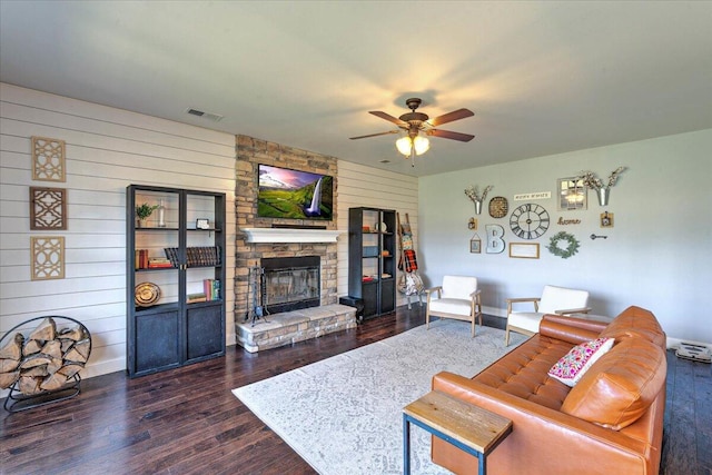 living area with visible vents, wood walls, a fireplace, dark wood-type flooring, and a ceiling fan
