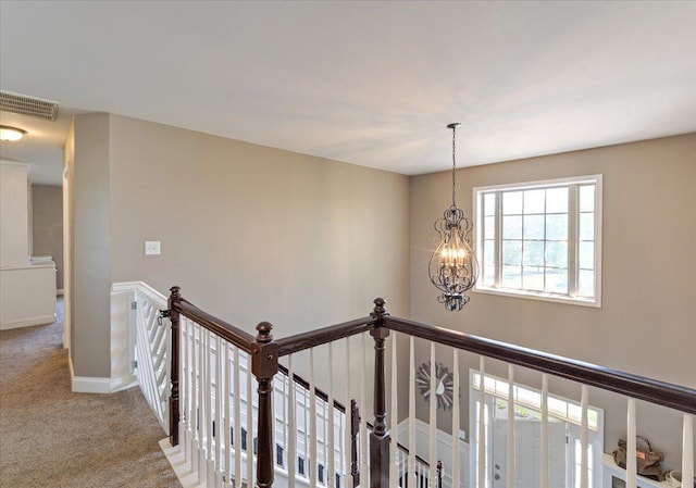 hall with visible vents, baseboards, carpet, a notable chandelier, and an upstairs landing