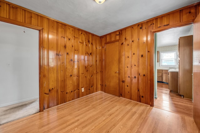 unfurnished room with baseboards, wood finished floors, wooden walls, and a sink