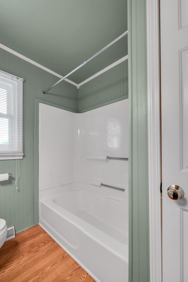 bathroom featuring wood finished floors, bathing tub / shower combination, toilet, visible vents, and crown molding