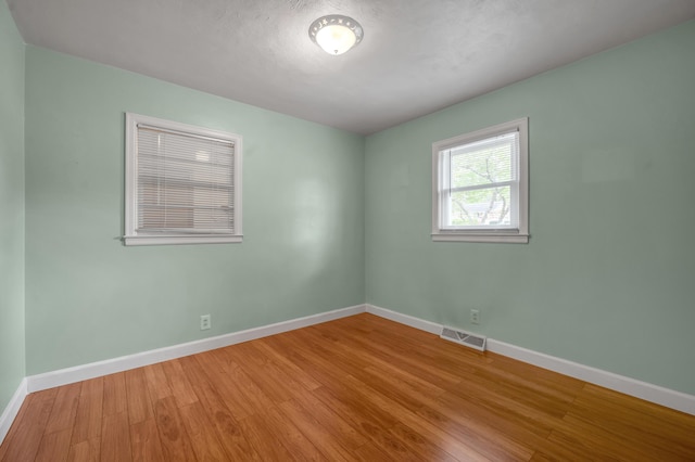 spare room with baseboards, visible vents, and wood finished floors