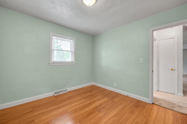 unfurnished room featuring light wood-type flooring, visible vents, and baseboards