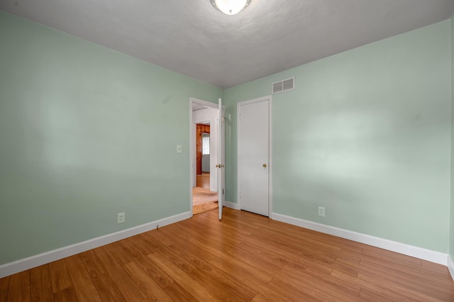empty room with light wood-type flooring, visible vents, and baseboards