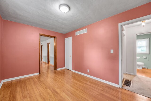 spare room featuring light wood finished floors, visible vents, and baseboards