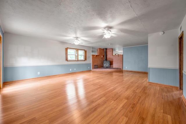 unfurnished living room with visible vents, a wood stove, ceiling fan, and light wood finished floors