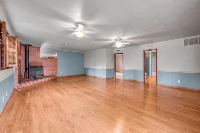 unfurnished living room with visible vents, a wood stove, a ceiling fan, and light wood-style floors