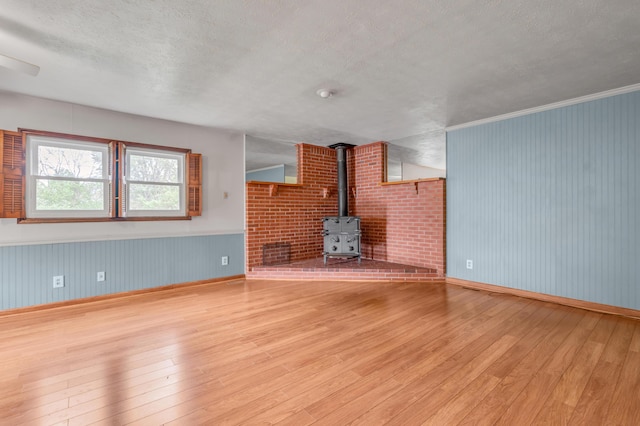 unfurnished living room with baseboards, a wood stove, hardwood / wood-style flooring, and a textured ceiling