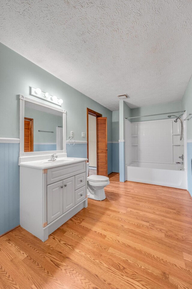 bathroom with wood finished floors, toilet, vanity, visible vents, and a textured ceiling