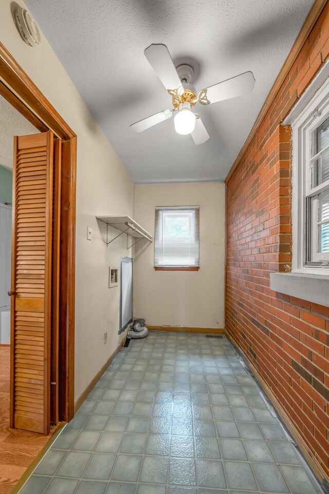 washroom featuring laundry area, brick wall, baseboards, a ceiling fan, and a textured ceiling