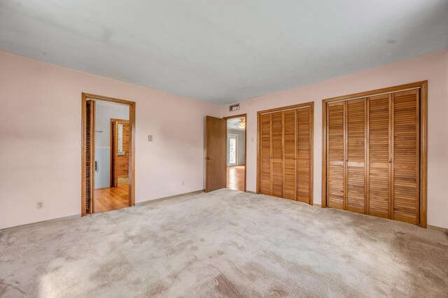 unfurnished bedroom with visible vents, carpet, and two closets