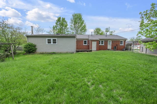 rear view of house with brick siding, a yard, and fence