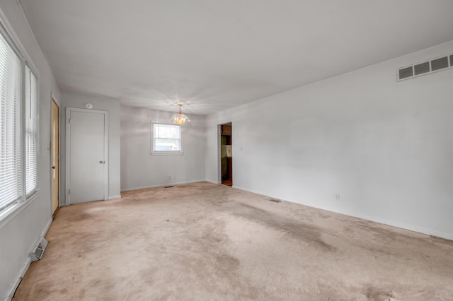 carpeted empty room with an inviting chandelier, visible vents, and baseboards