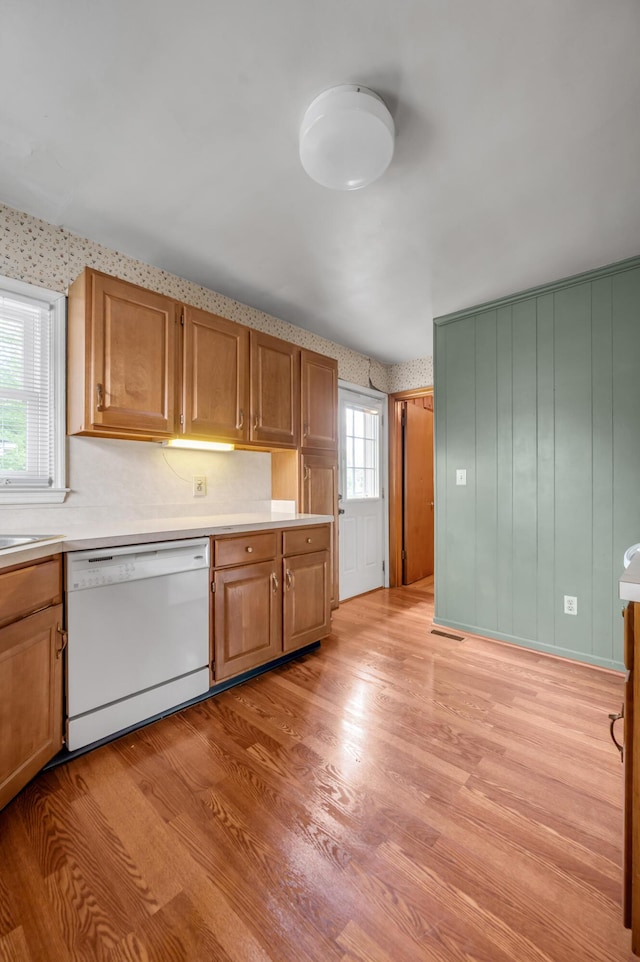kitchen with brown cabinetry, light wood-style floors, light countertops, and white dishwasher