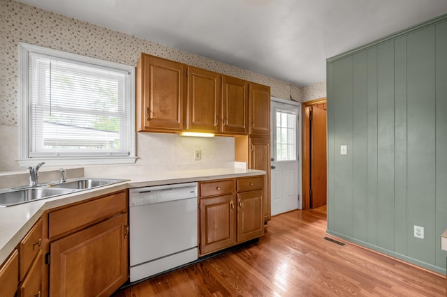 kitchen with a sink, visible vents, light countertops, dishwasher, and wallpapered walls