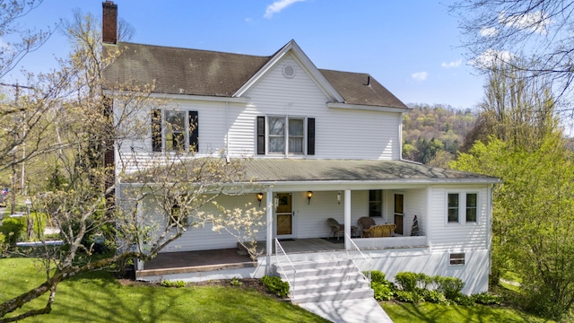 country-style home featuring a chimney, a porch, a shingled roof, and a front lawn