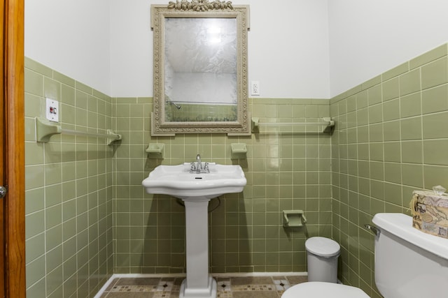 half bathroom with toilet, a wainscoted wall, tile patterned flooring, and tile walls