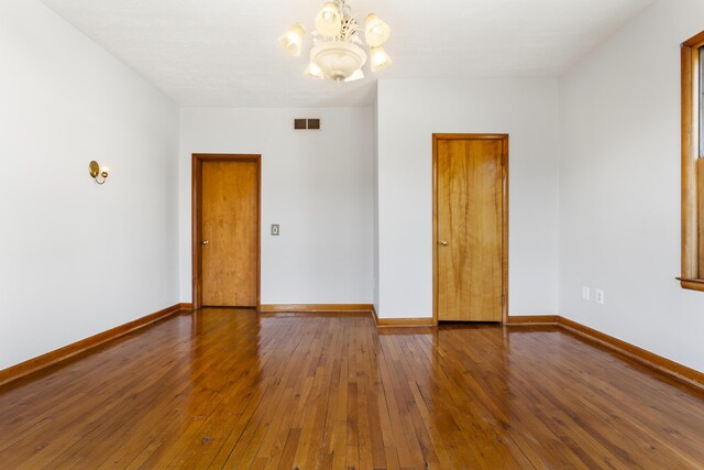 spare room featuring visible vents, hardwood / wood-style flooring, a notable chandelier, and baseboards