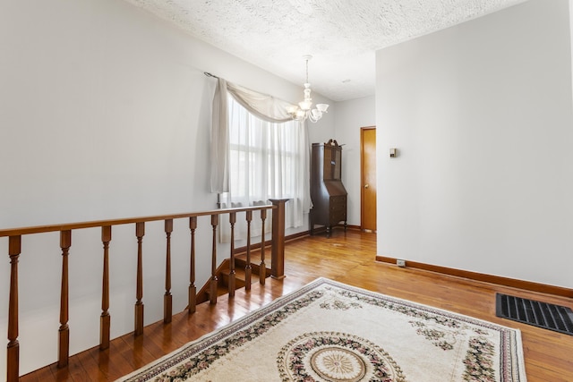 staircase featuring wood finished floors, an inviting chandelier, baseboards, visible vents, and a textured ceiling