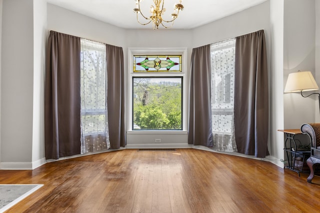 unfurnished dining area with visible vents, a notable chandelier, hardwood / wood-style floors, and baseboards