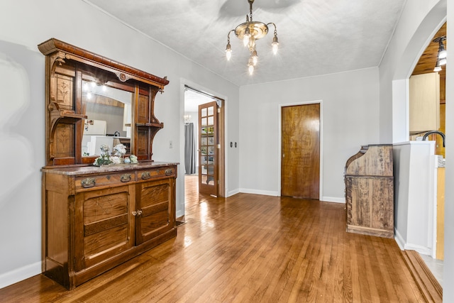 interior space with arched walkways, an inviting chandelier, hardwood / wood-style floors, and baseboards