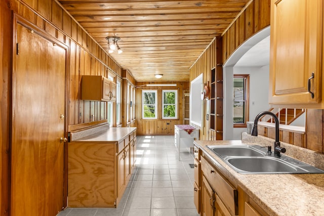 kitchen featuring arched walkways, wood ceiling, light tile patterned floors, light countertops, and a sink